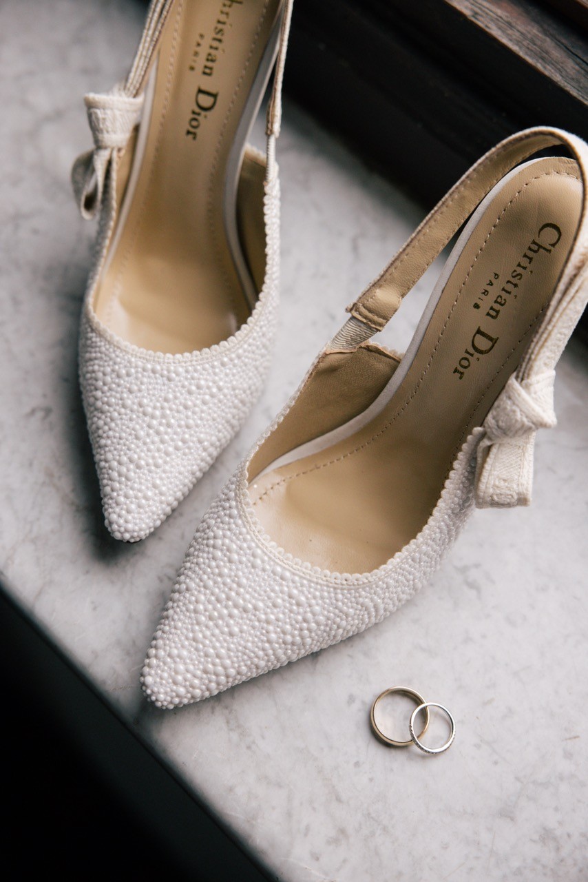 Scarpe da sposa bianche con perline e fedi nuziali sul marmo, dettagli dei preparativi al Castello di Tabiano