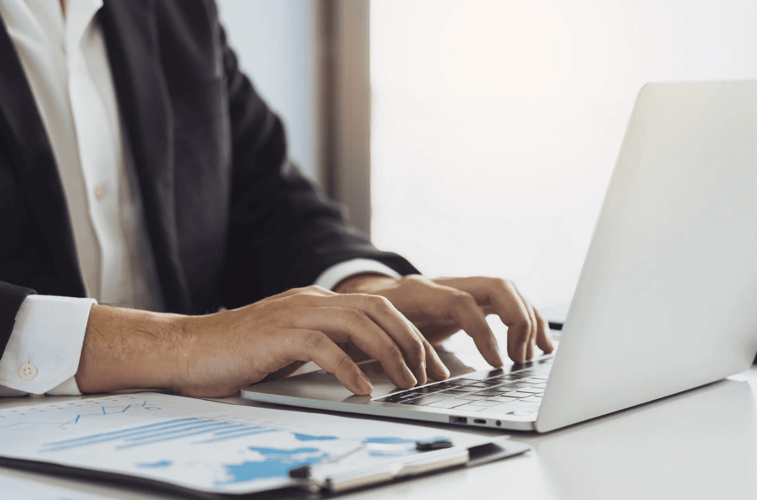 Business professional typing on a laptop next to performance reports, illustrating real-time Amazon FBA budget reallocation during peak sales windows.
