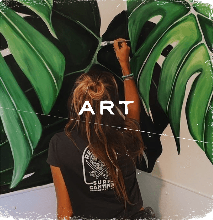 Rustic photograph of a young woman  painting large jungle flora mural labeled 'Art'