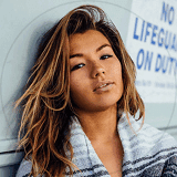 A woman in a striped sweater leans casually against a wall, showcasing a relaxed and stylish pose.