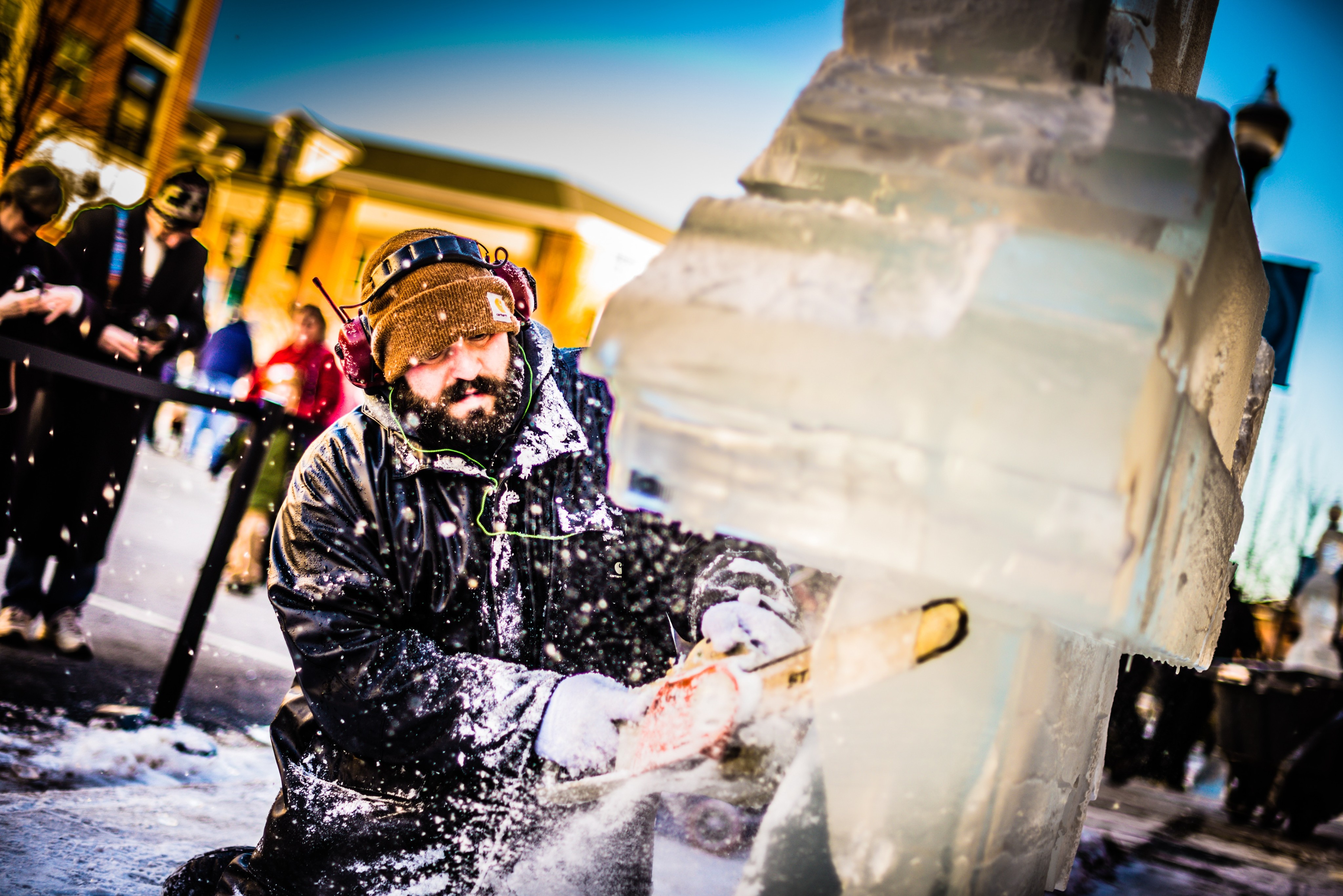 man carving ice with a chainsaw as ice bounces off of his beard