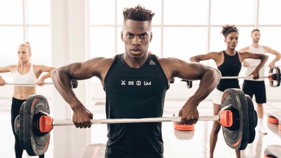 Athletische Gruppe trainiert synchron aufrechtes Rudern mit Langhanteln.