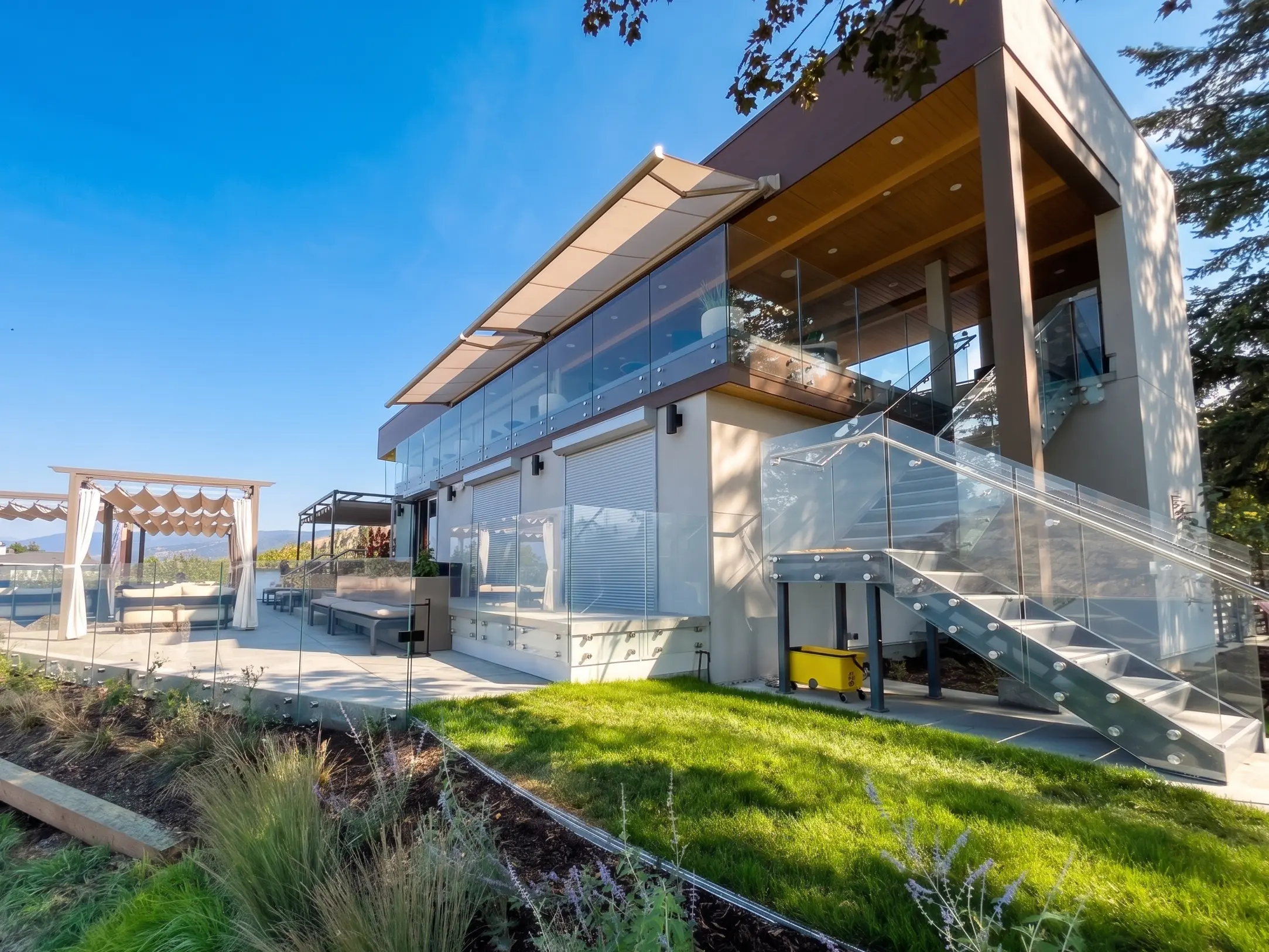 Multi-level Parksville home with wrap-around glass railings, pergola-covered deck seating, and an exterior glass staircase under a clear Vancouver Island sky.