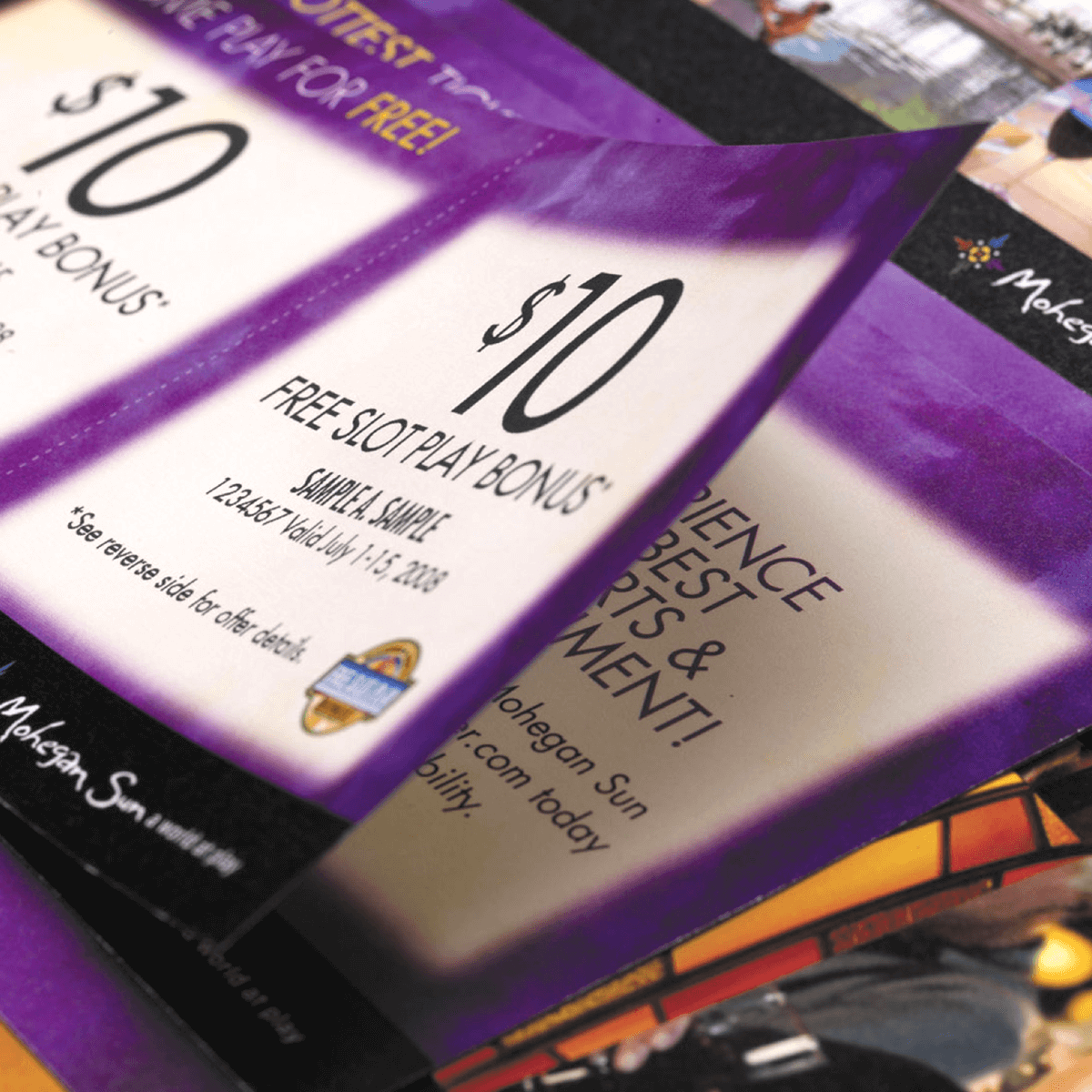 A close-up of two "$10 Free Slot Play Bonus" coupons from Mohegan Sun, featuring purple borders and printed text with terms and conditions visible.