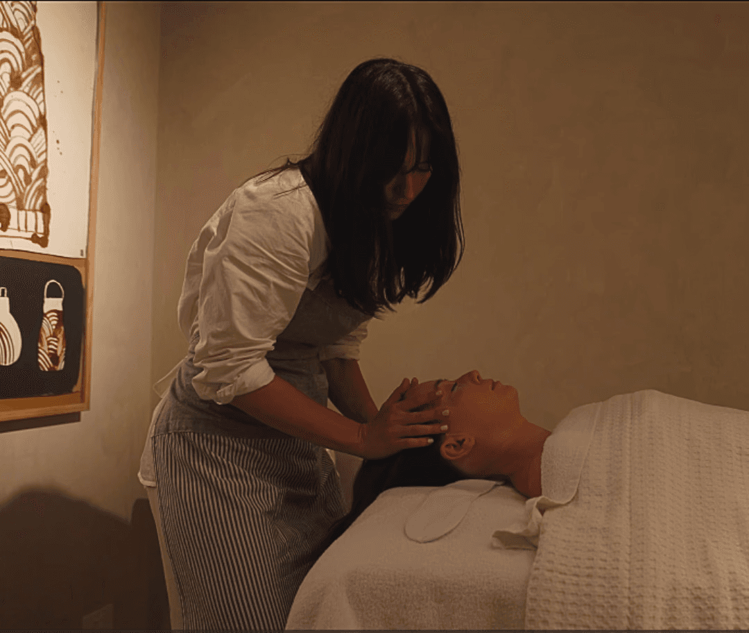 A woman performing a facial treatment on another woman lying peacefully, focused on relaxation and skincare.