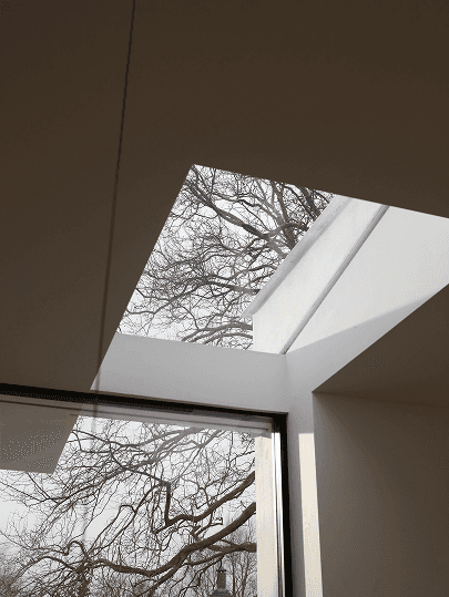 Binnenlichtkoepels omlijsten kale boomtakken tegen een bewolkte hemel en brengen natuurlijk licht diep in een woning in Knokke.