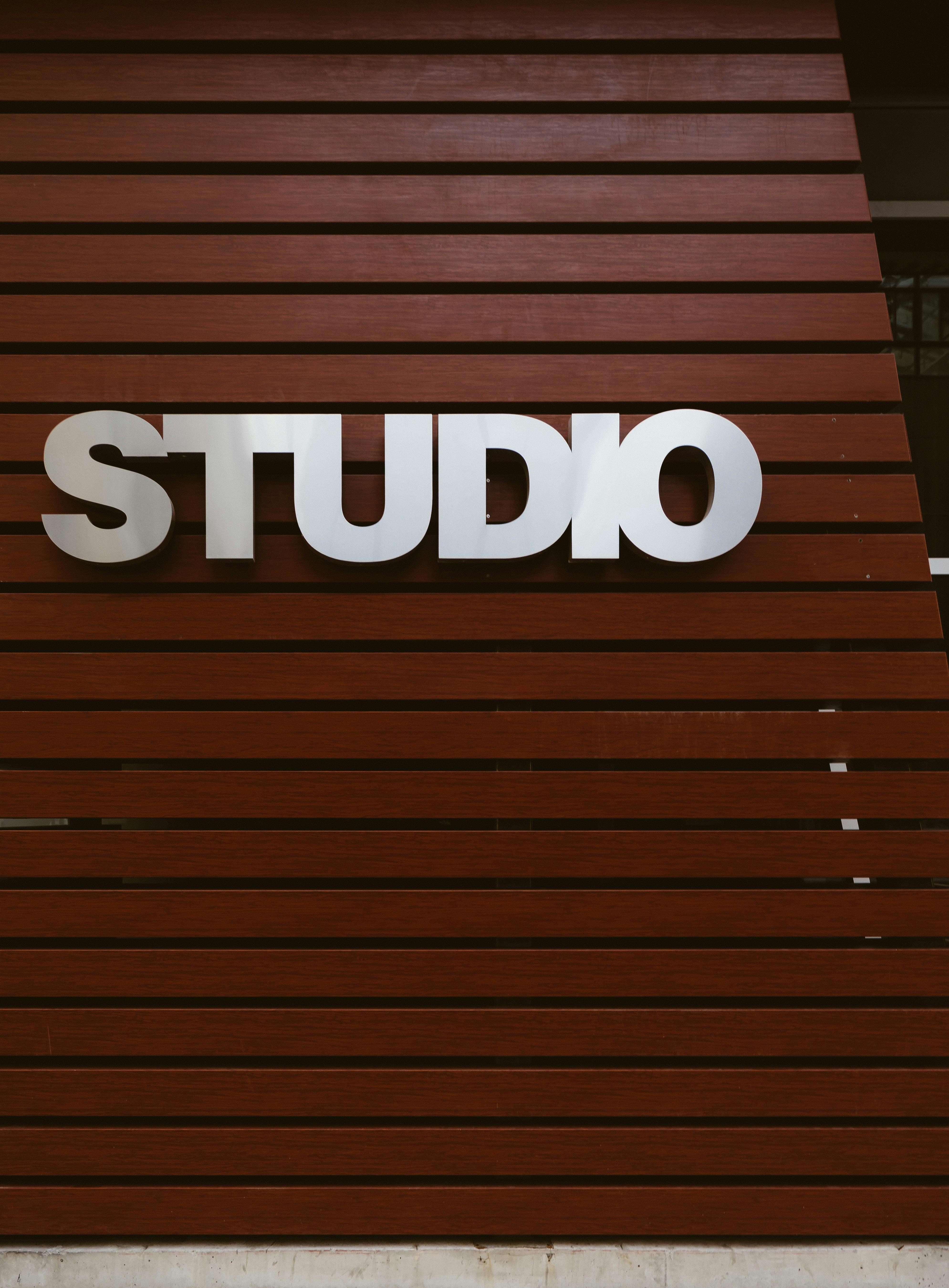 Silver "STUDIO" sign on a brown wooden slatted wall.