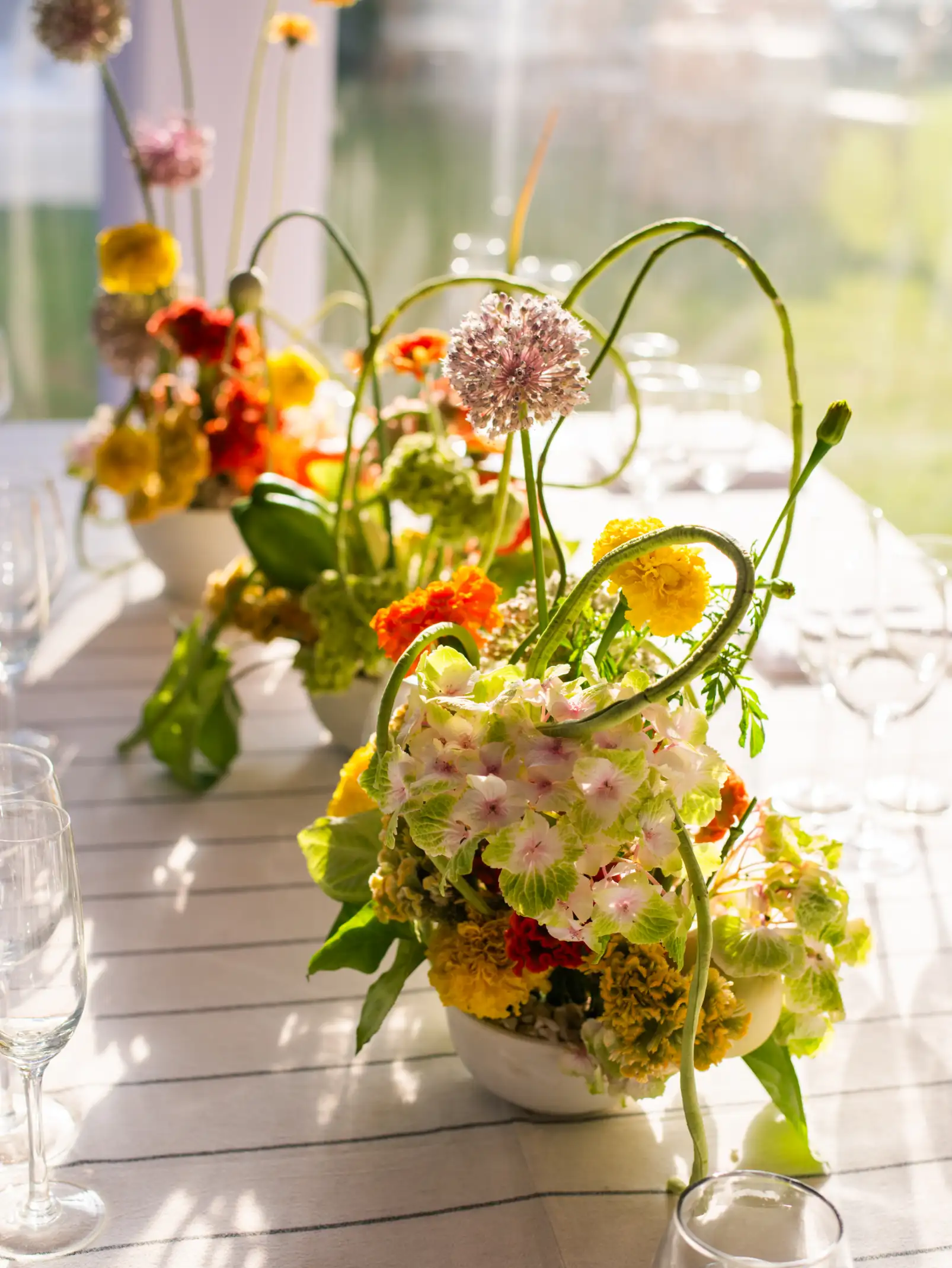 Centro de mesa con flores coloridas y formas orgánicas en tonos amarillos, naranjas y verdes iluminado por la luz del sol.