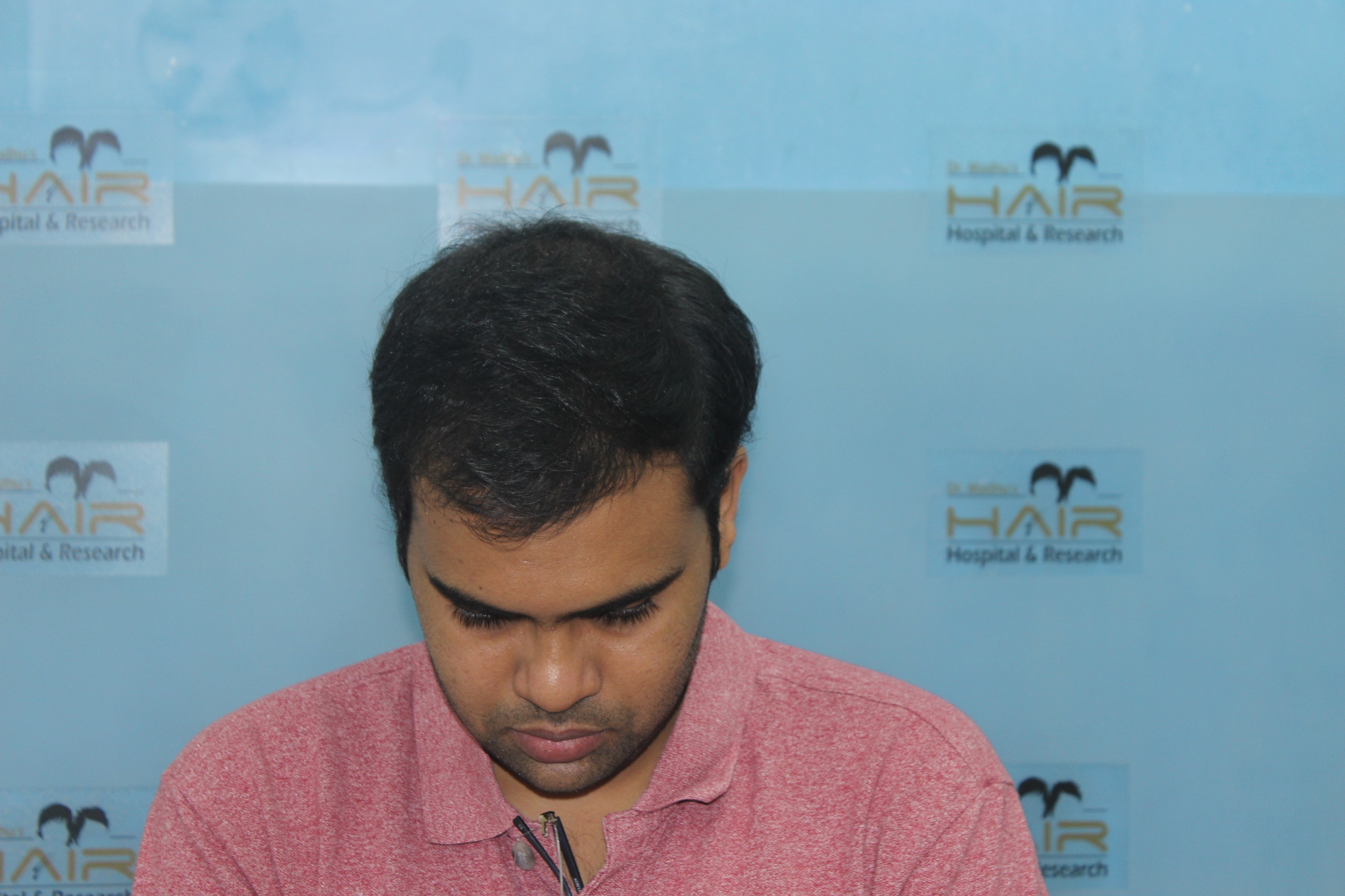 Smiling person in bucket hat outdoors with trees, building, and blue sky in background