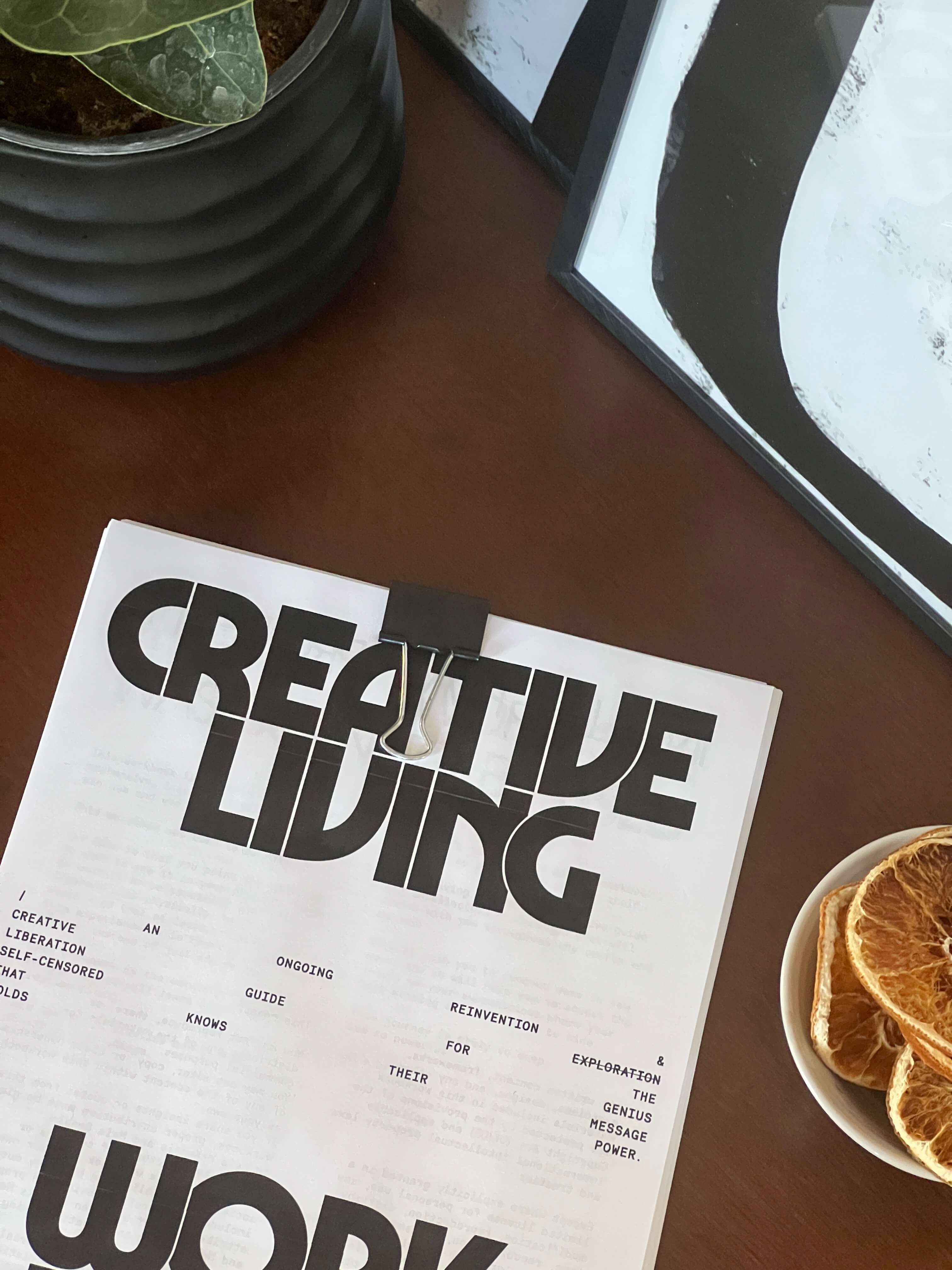 A stack of papers titled creative living held together with a binder clip on a dark wood table