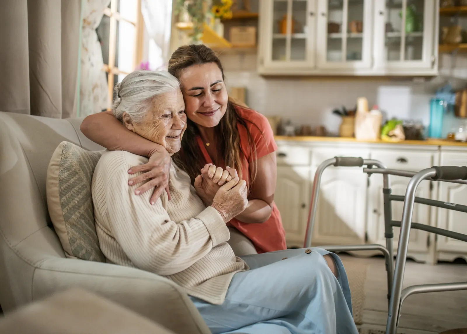 A daughter with her arm around her mother at home, a walker beside them