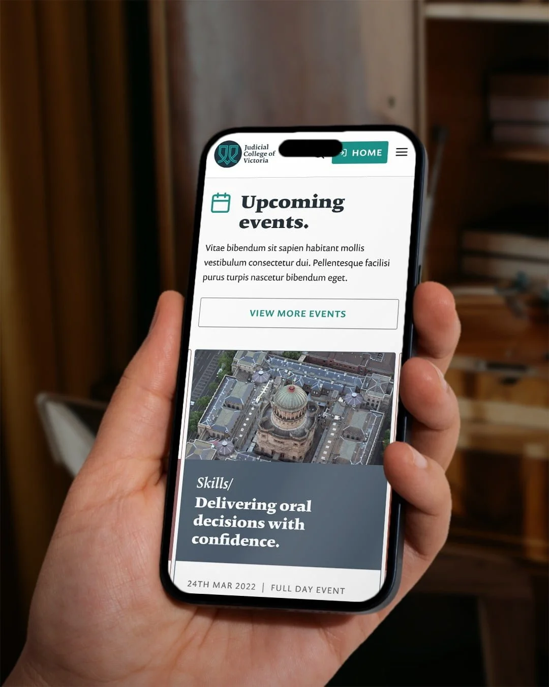 Hand holding a phone showing the Wisdom Shared 'Upcoming events' page, with the Judicial College of Victoria logo