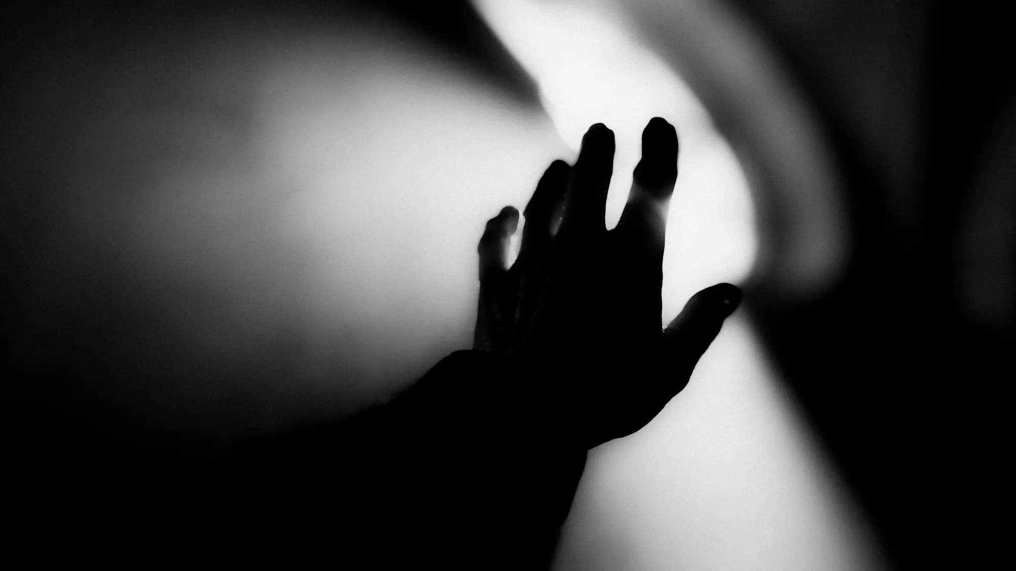 Black-and-white silhouette of a hand reaching into the light