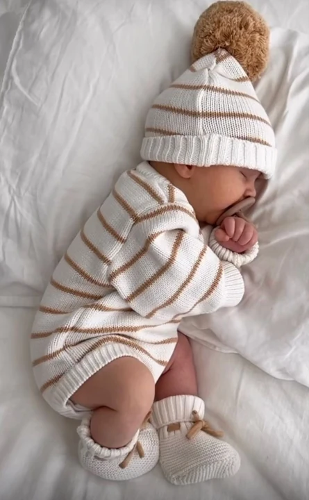 Sleeping newborn in a striped outfit and pompom hat