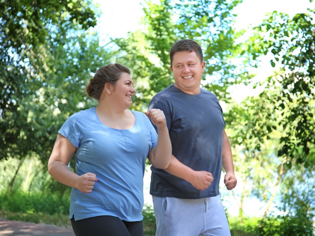 plus-sized couple achieving weight loss from running on a gentle route in a park near a pond