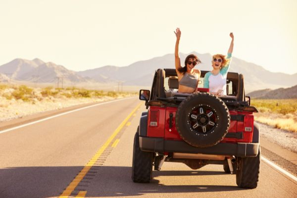 Two girls laughing and singing in a Jeep as music plays, capturing the carefree joy of a summer road trip.