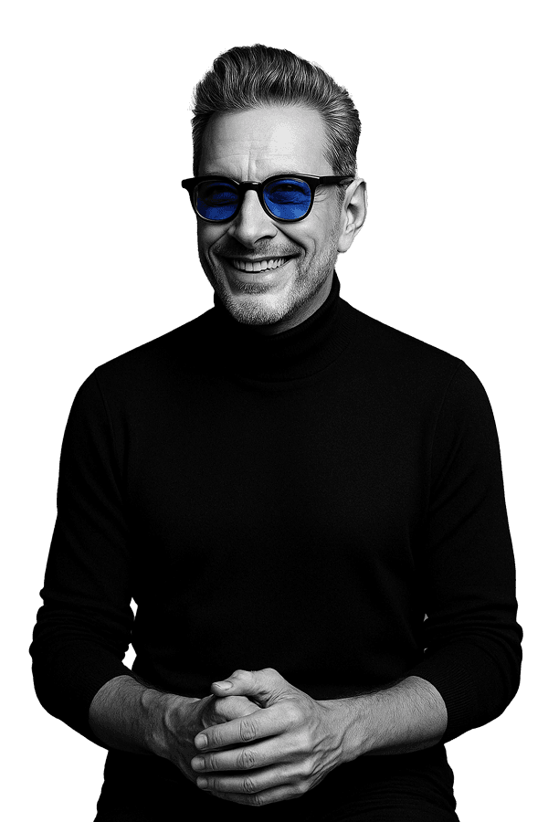Black-and-white studio portrait of a smiling man in a black turtleneck with cobalt-blue lenses, hands loosely clasped.