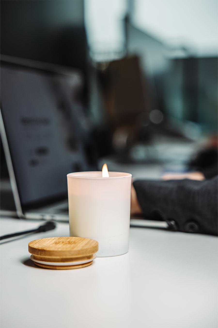 A lit white candle with a blurred laptop screen in the background