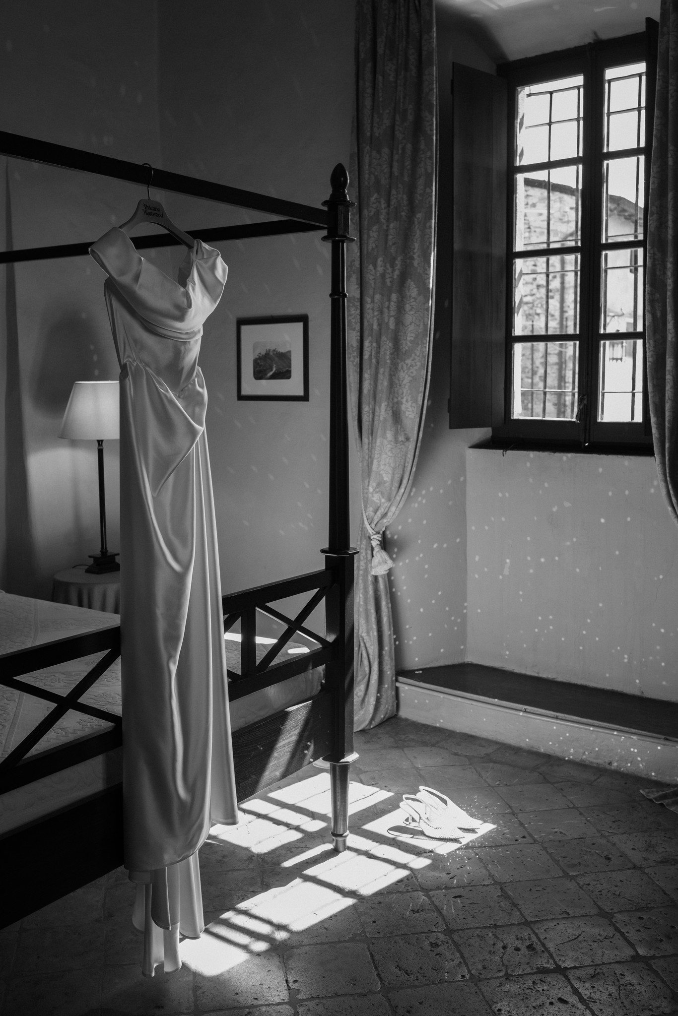Abito da sposa appeso al letto a baldacchino, luce naturale dalla finestra al Castello di Scipione, preparativi matrimonio