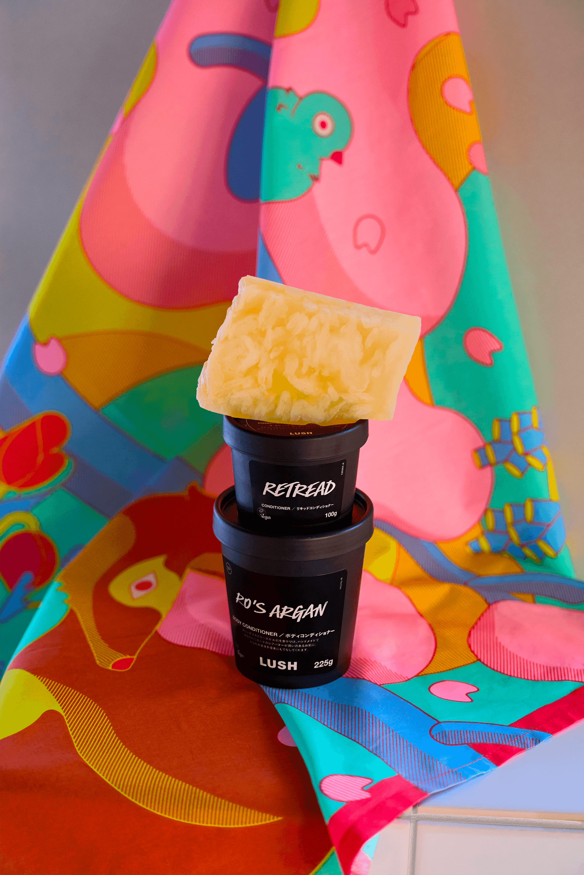 Stack of Lush product containers and bath items displayed against a backdrop of illustrated fabric with spring motifs.