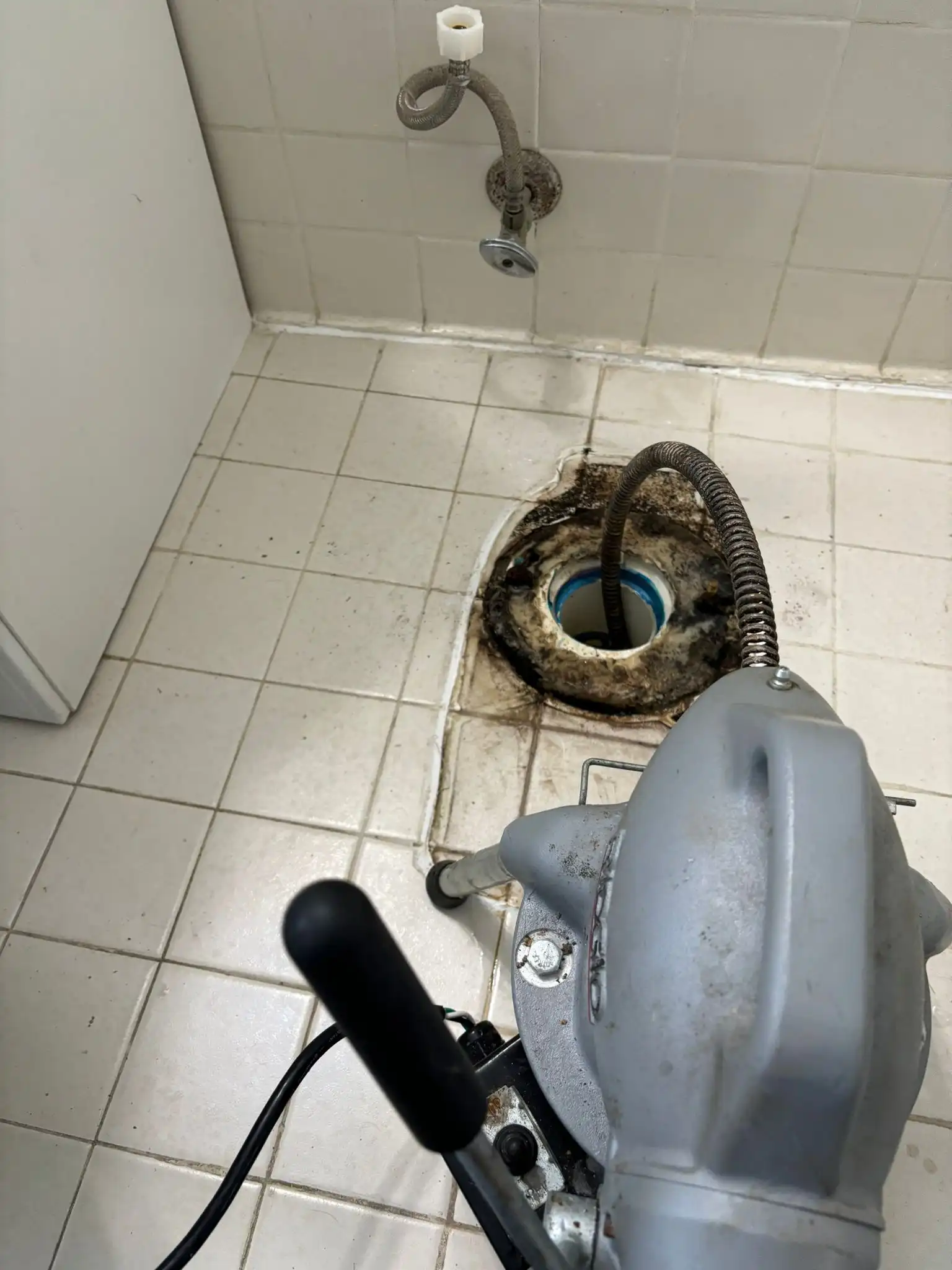 A drain snake machine clearing a main line blockage through an exposed closet flange during a professional toilet repair.
