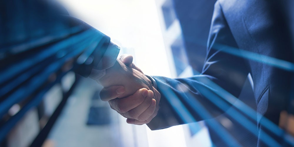 A close-up of two hands shaking, symbolizing partnership and collaboration, with a blue digital background.