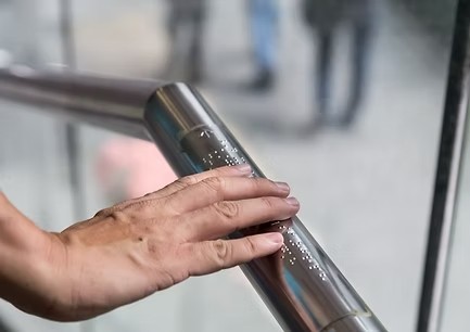Eine Hand ertastet Blindenschrift (Braille) auf einem Handlauf – Unterstützung des Blindenhilfswerks Berlin durch die DAG.