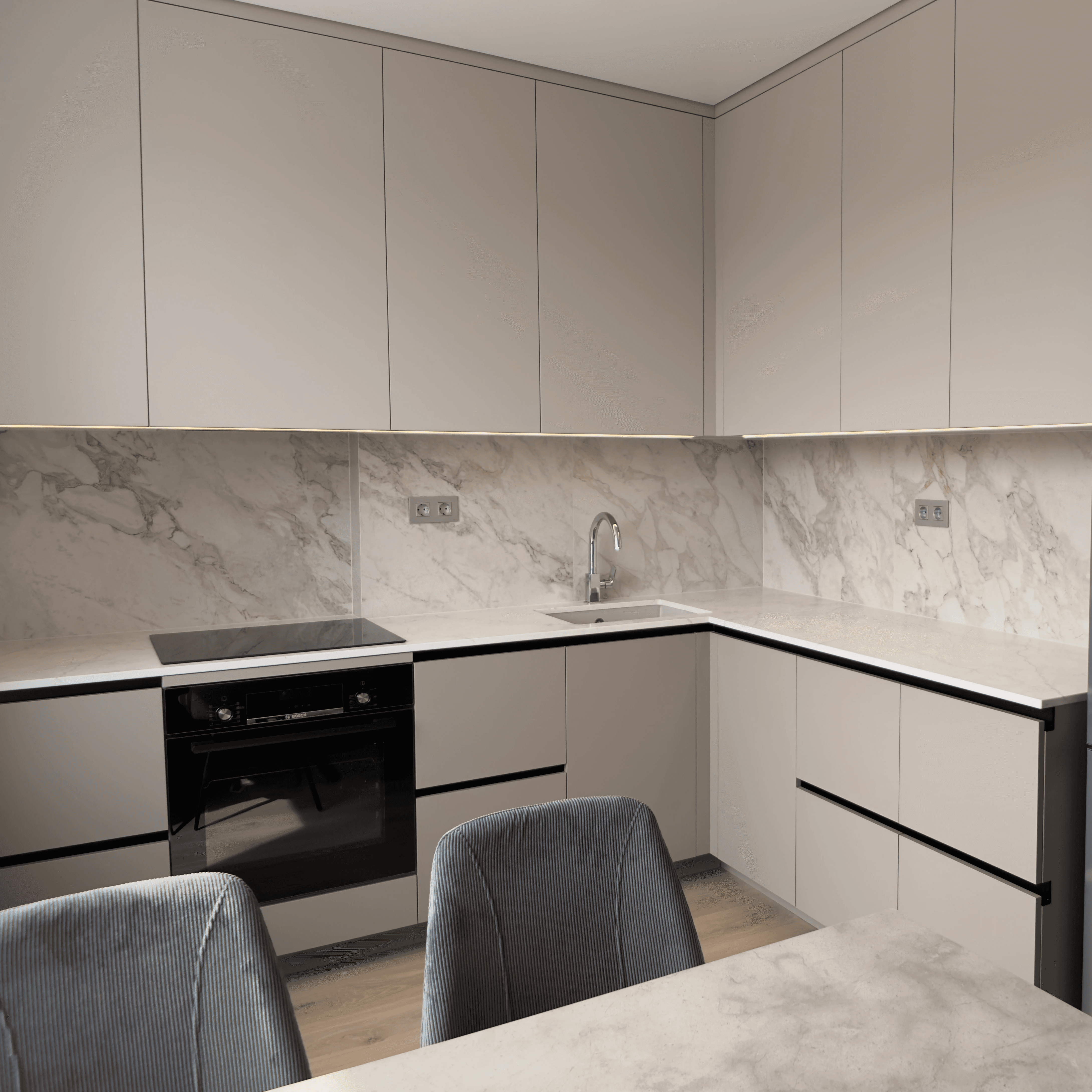 Кутова кухня з мармуровим фартухом, сірими фасадами та великою кількістю місць для зберігання