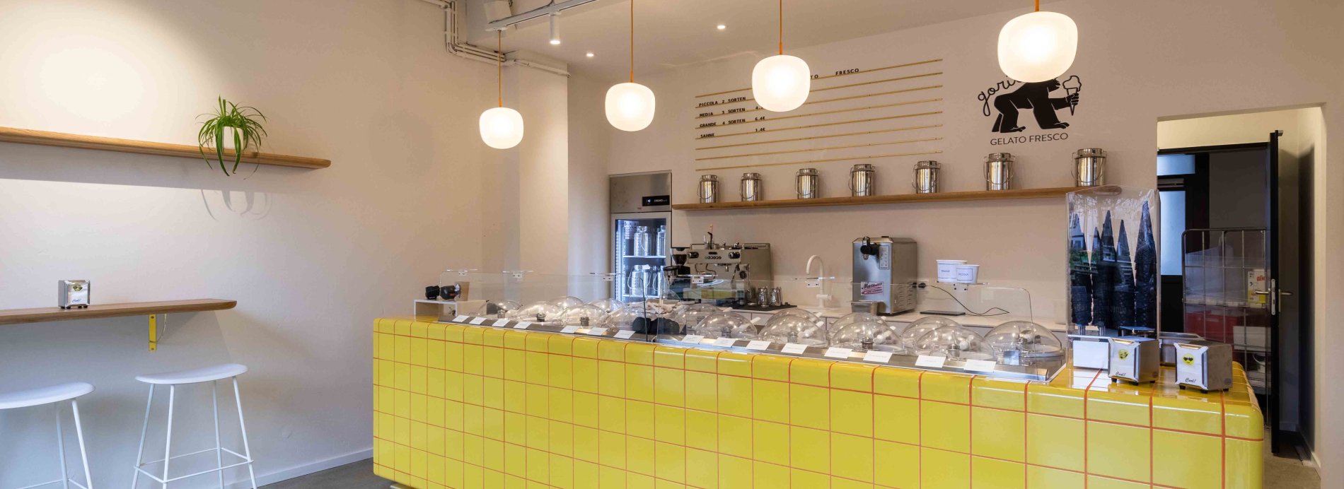 Modernes Café-Interieur mit gelber Theke, Barhockern und hängenden Lampen.