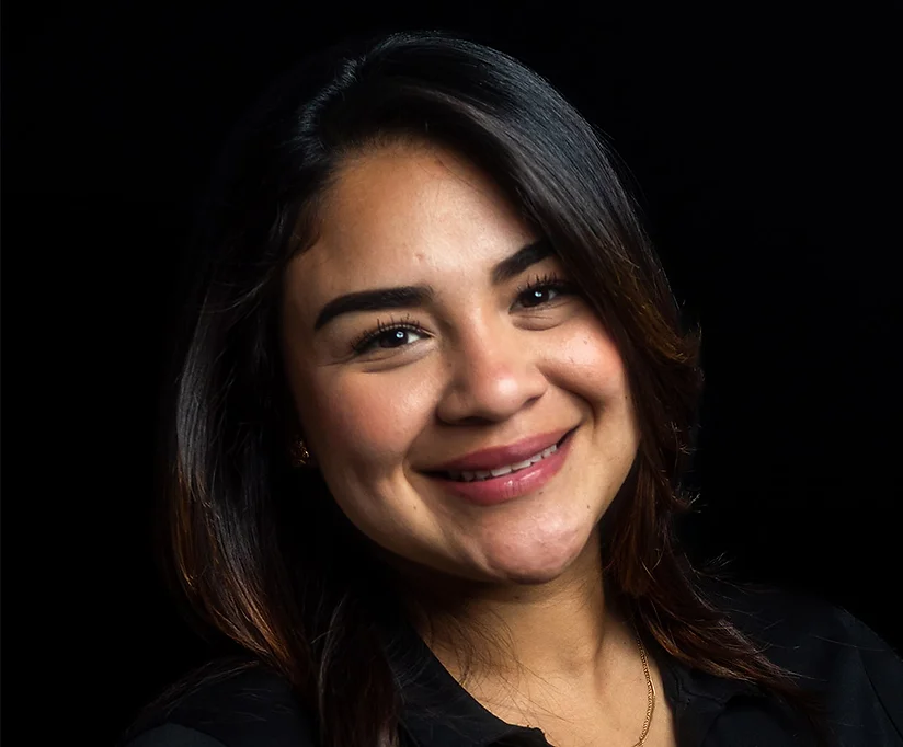 Mujer con el pelo oscuro sonriendo contra un fondo negro.