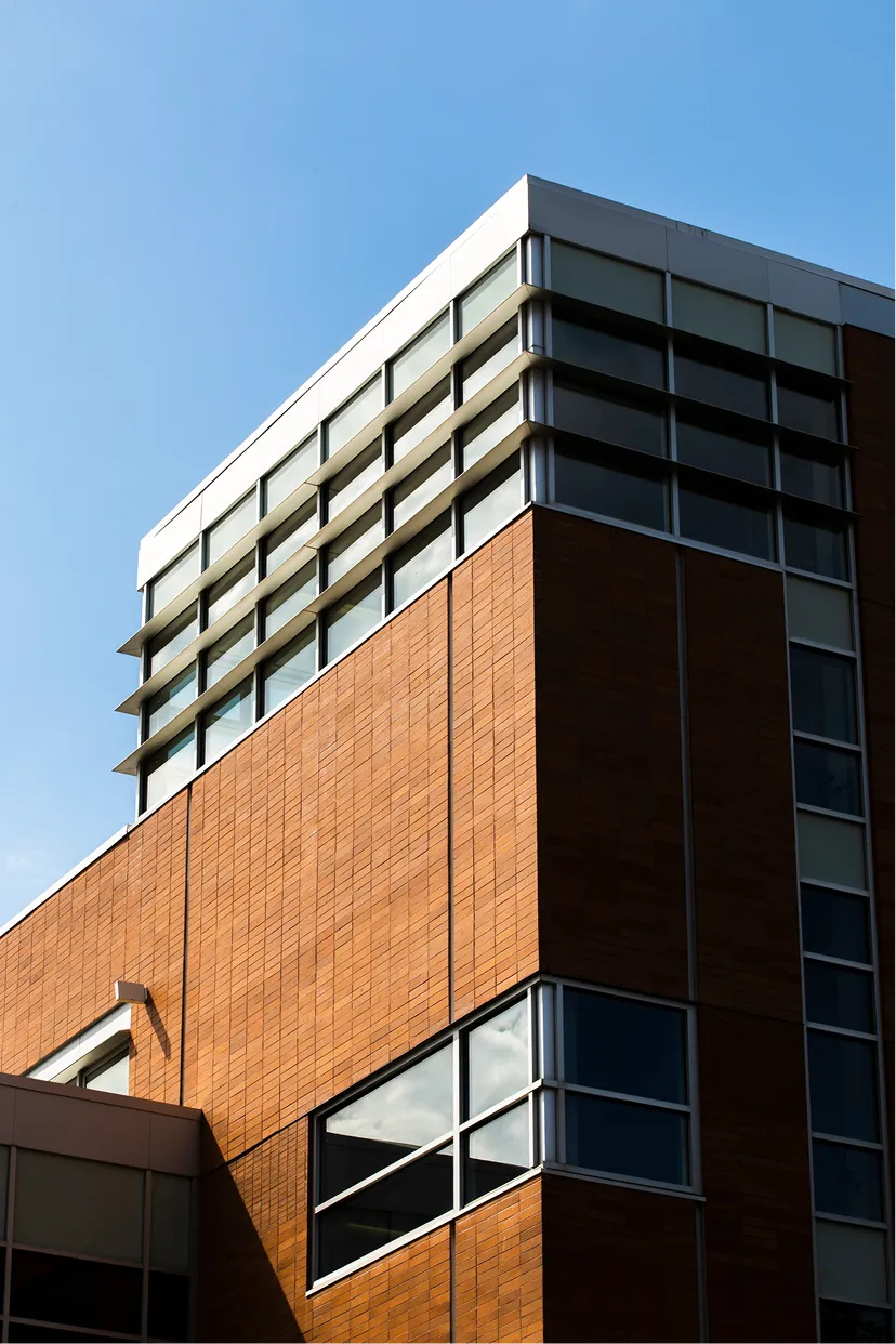 Low-angle view of a modern brick corporate building featuring glass windows and horizontal architectural louvers.