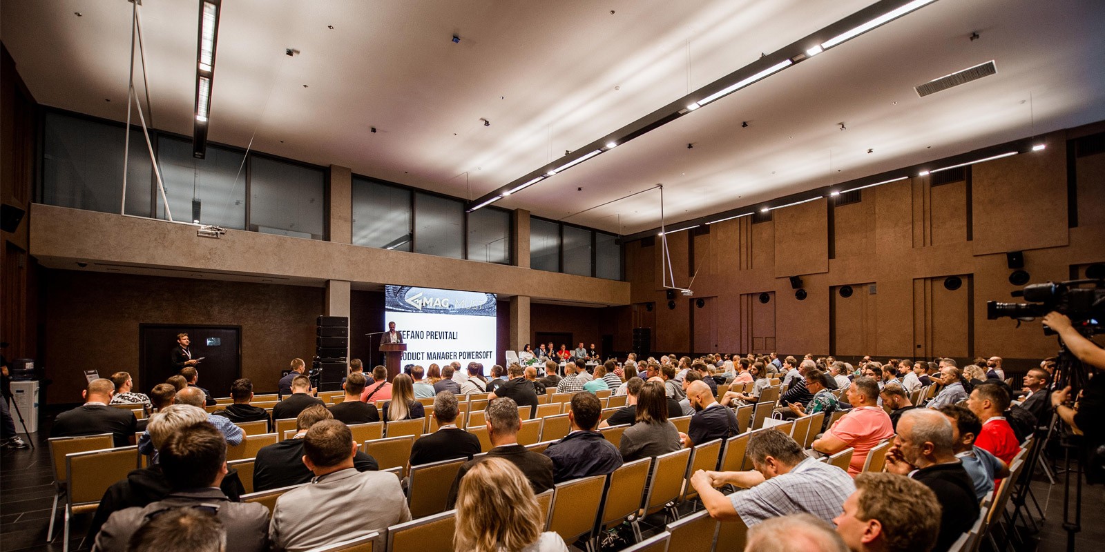 Conference audience watching a speaker on stage with projection screen