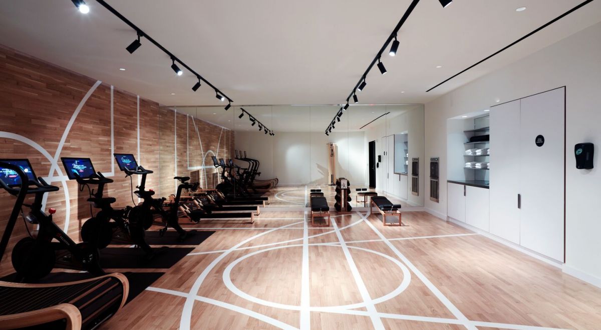 Modern hotel fitness room with exercise equiment, a floor-to-ceiling mirror and a wooden floor with athletic court markings that flow seamlessly onto an accent wall.