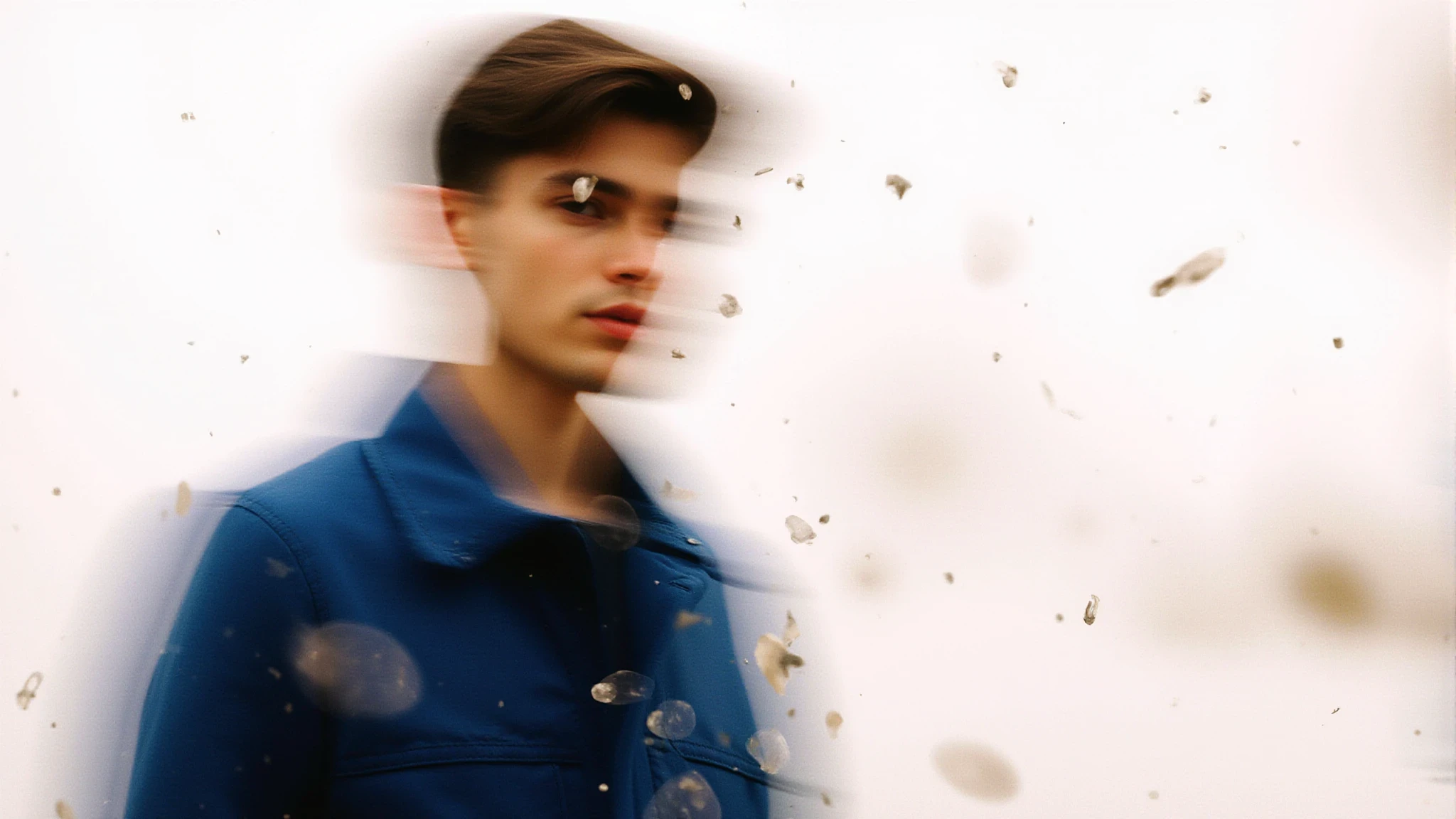 Blurred abstract image of a young man in a blue coat against a light background, creating a surreal and dreamlike effect.