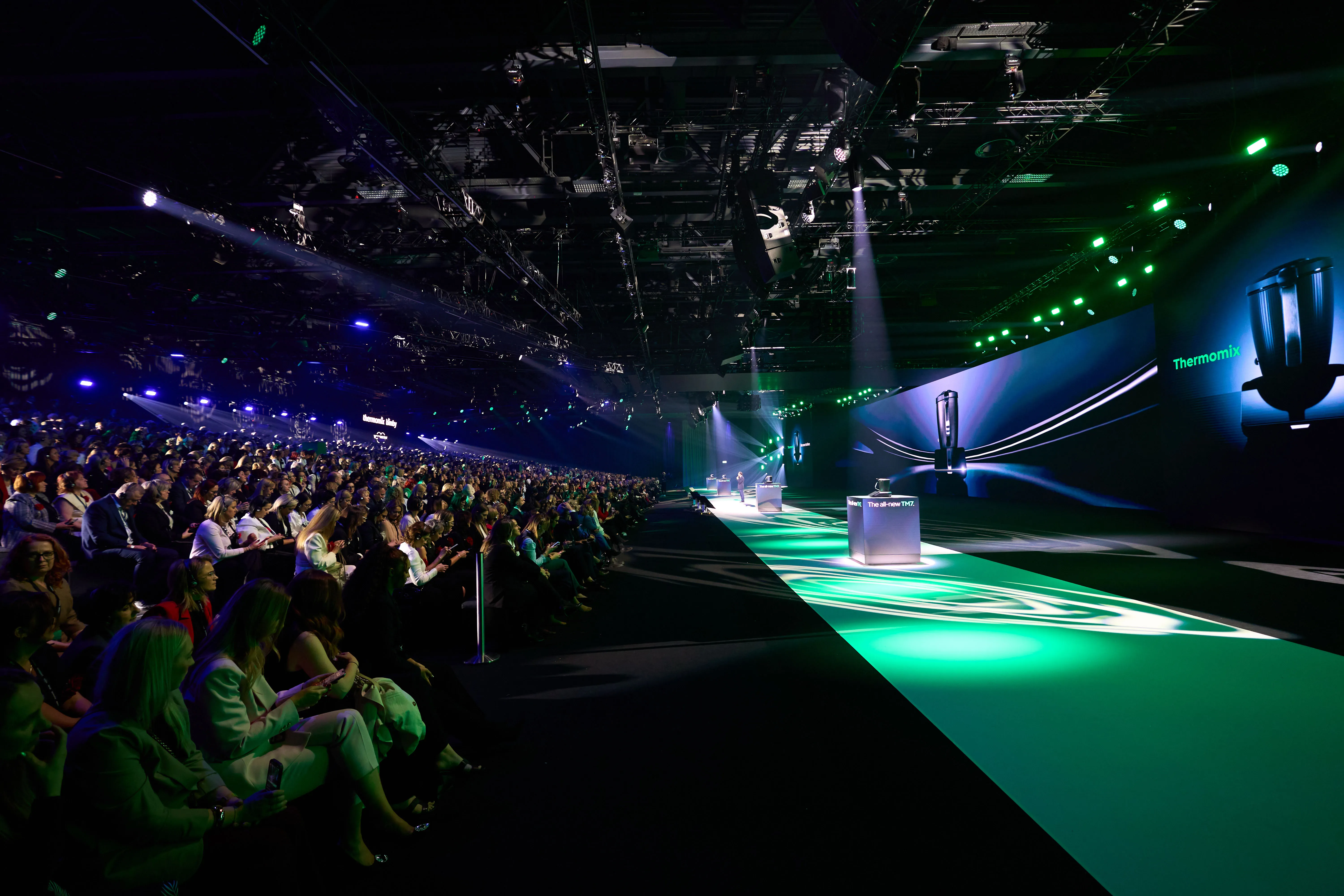 Audience along the runway with Thermomix appliances on pedestals in green light.
