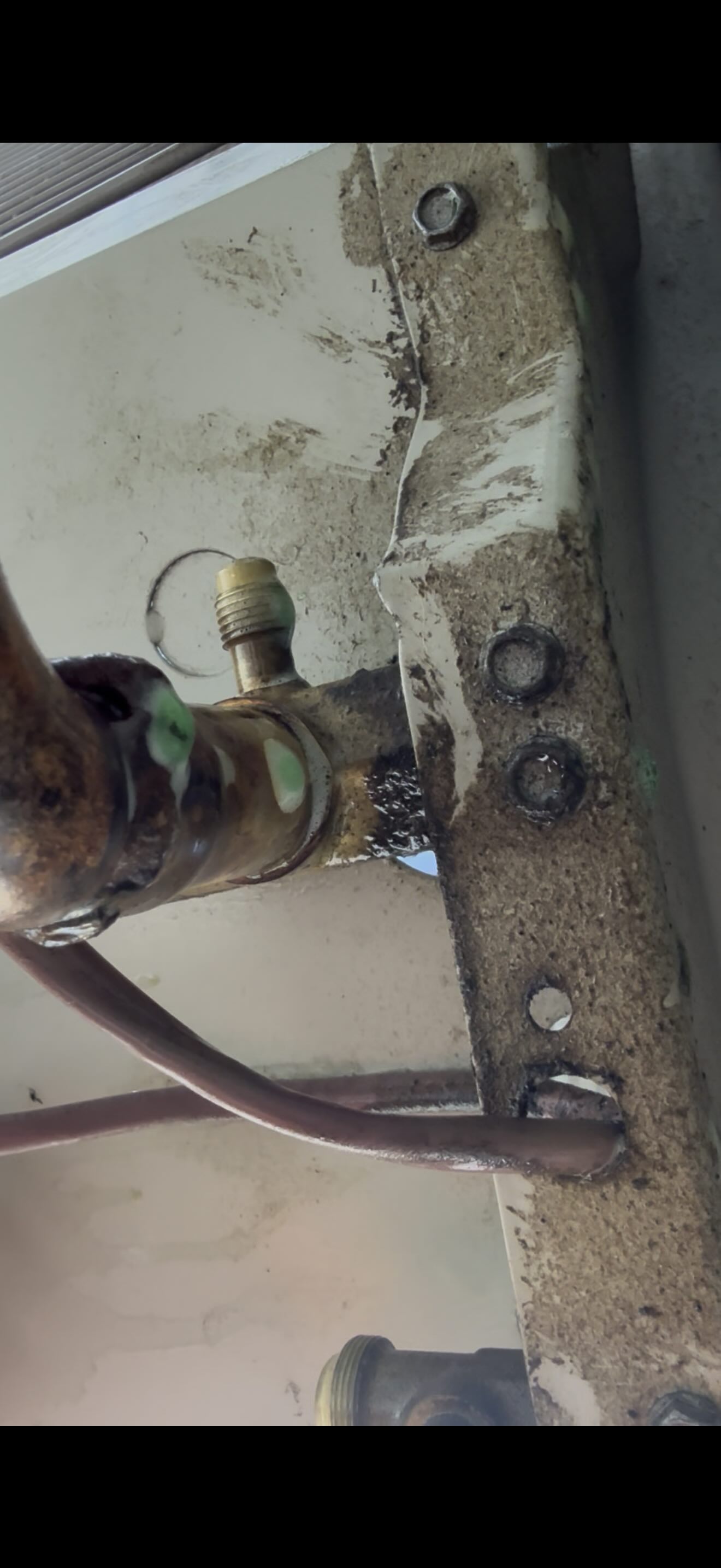 Oil-darkened braze joint at a suction-line service tee on an outdoor AC unit, the source of the refrigerant leak.