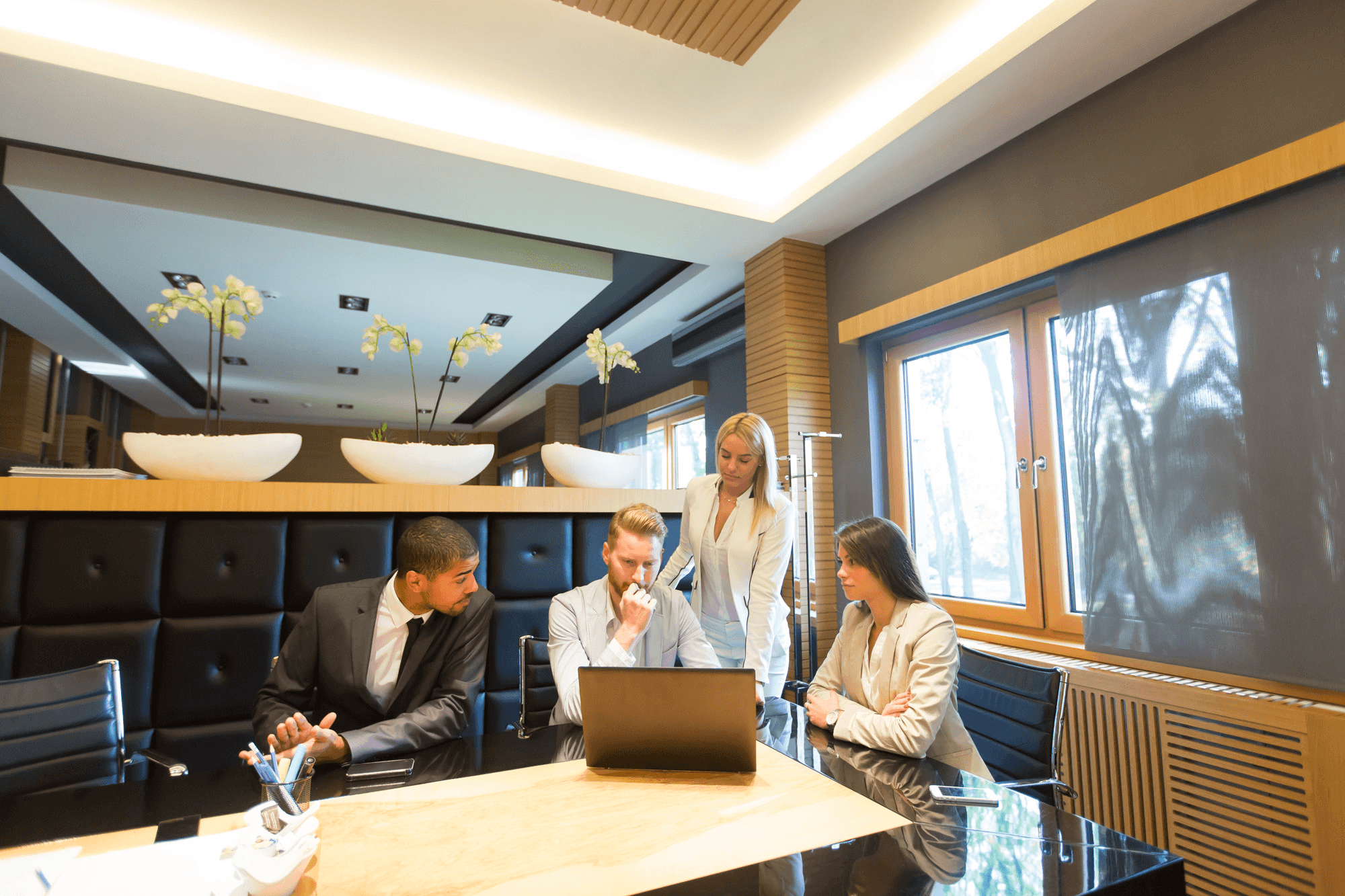 Four business professionals in a modern conference room collaborating around a laptop.