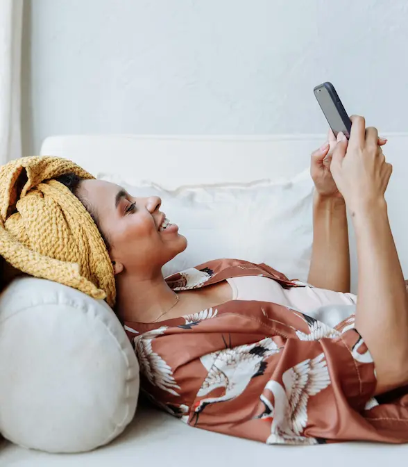 A woman relaxing on a couch at home, smiling while looking at her phone in a calm, unhurried moment.