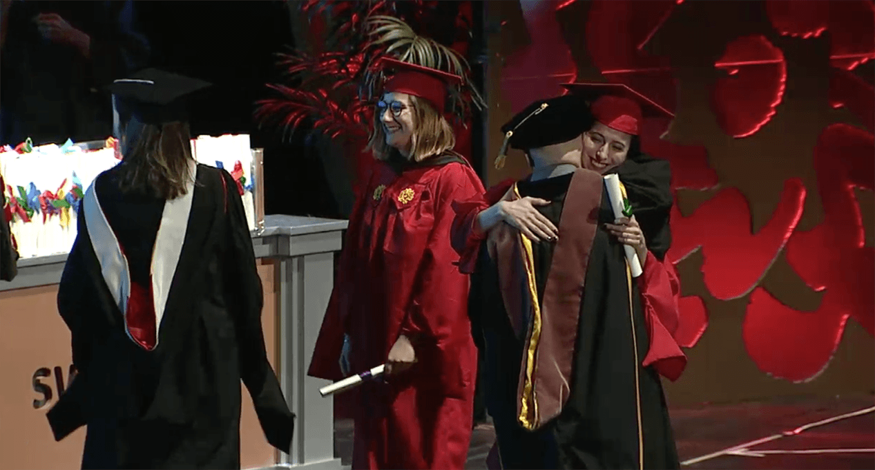 A photo of a couple of grad students and teachers hugging and congratulating each other.
