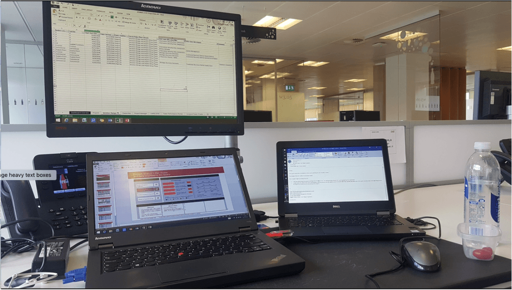 laptops on a desk with a monitor above