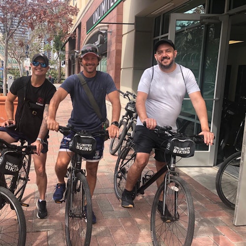 三个人在一家名为“无限骑行”的自行车租赁店外骑自行车，面带微笑，准备在阳光明媚的日子里出发。