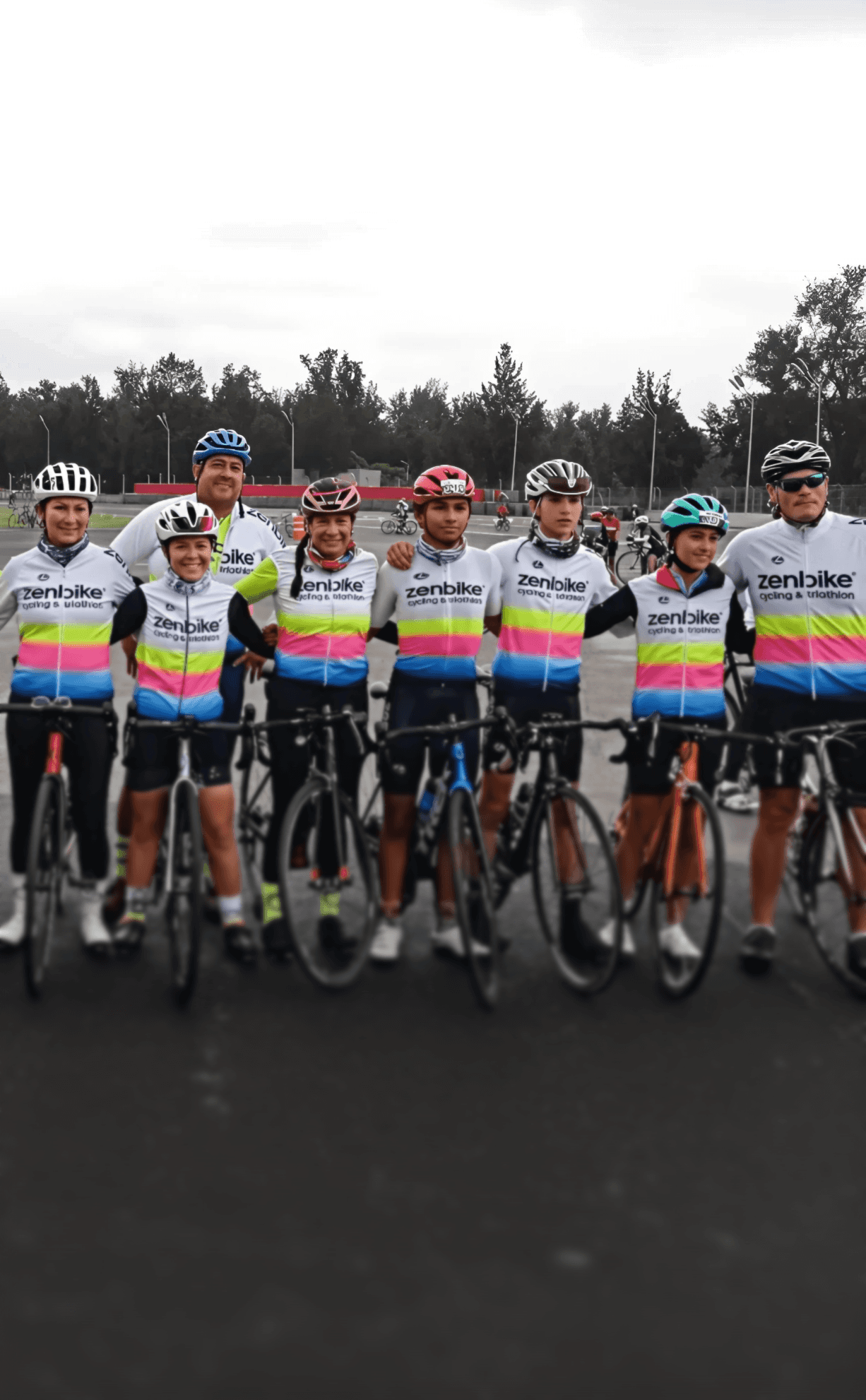 Equipo zenbike reunido sobre pista asfaltada en día nublado, usando uniformes oficiales en colores blanco, rosa, azul y amarillo.