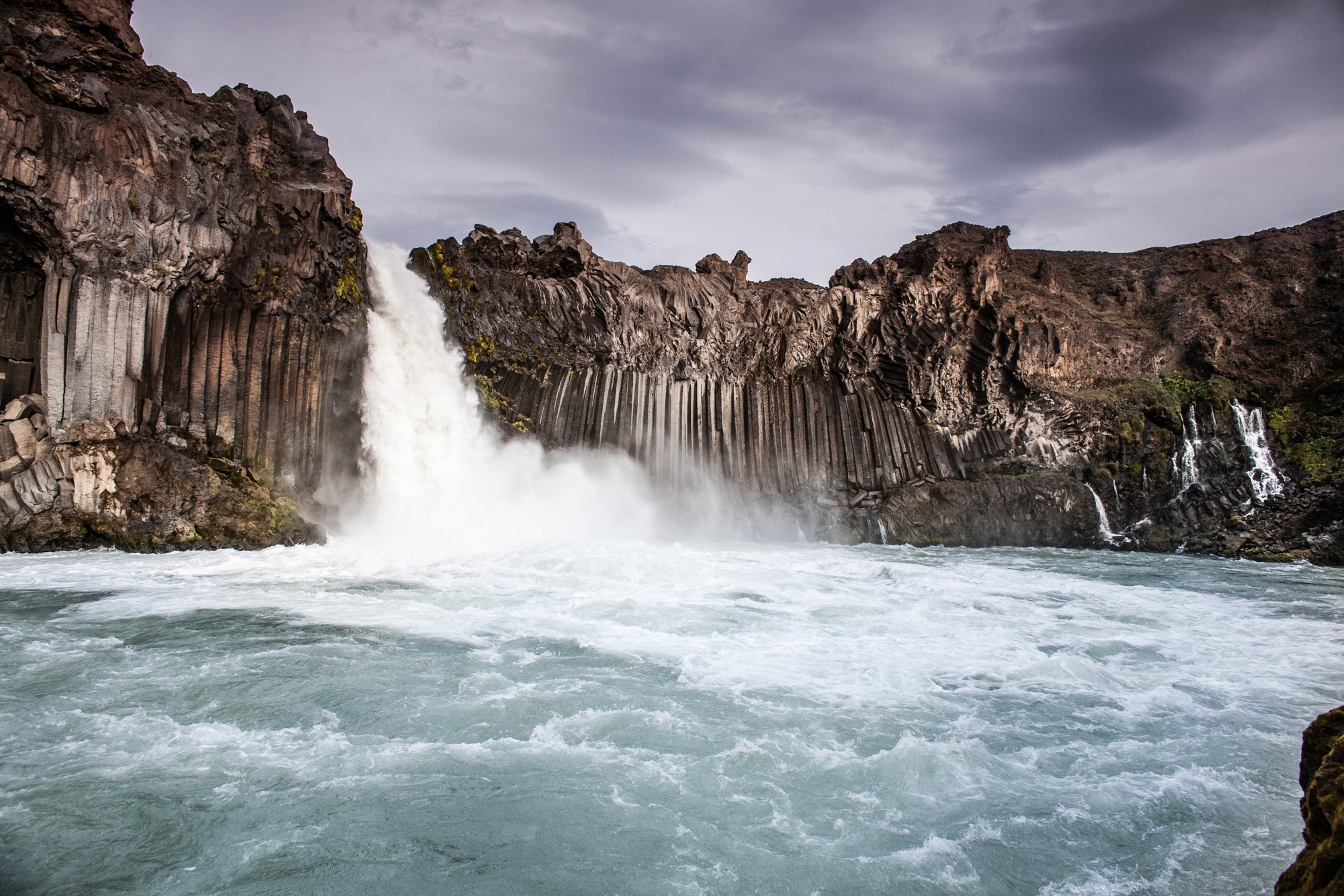 Goðafoss waterfall in North Iceland, a wide curved horseshoe-shaped cascade dropping over dark basalt rock into the river below