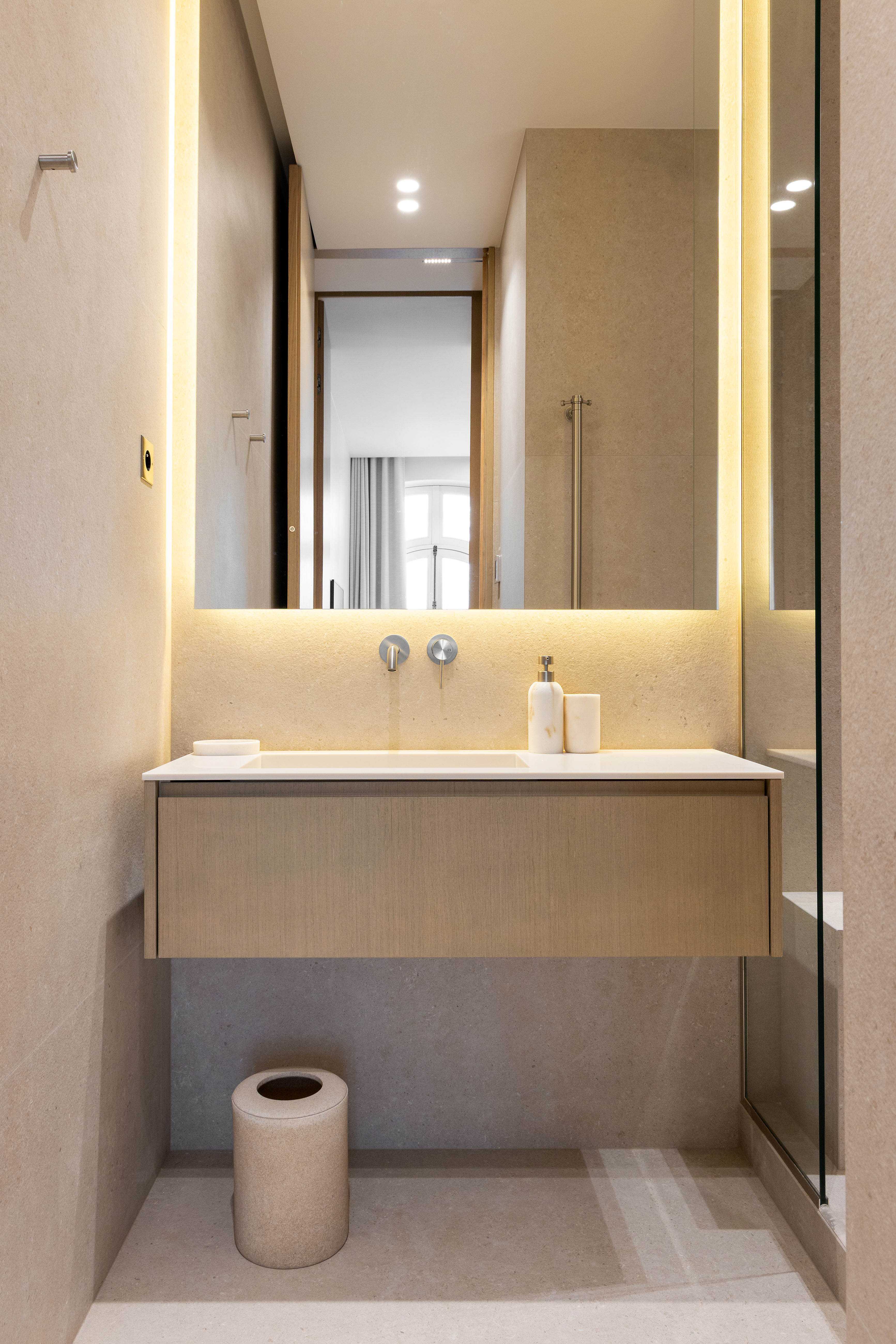 Salle de bain avec vasque suspendue en bois clair, miroir retro-eclaire et revetement pierre naturelle