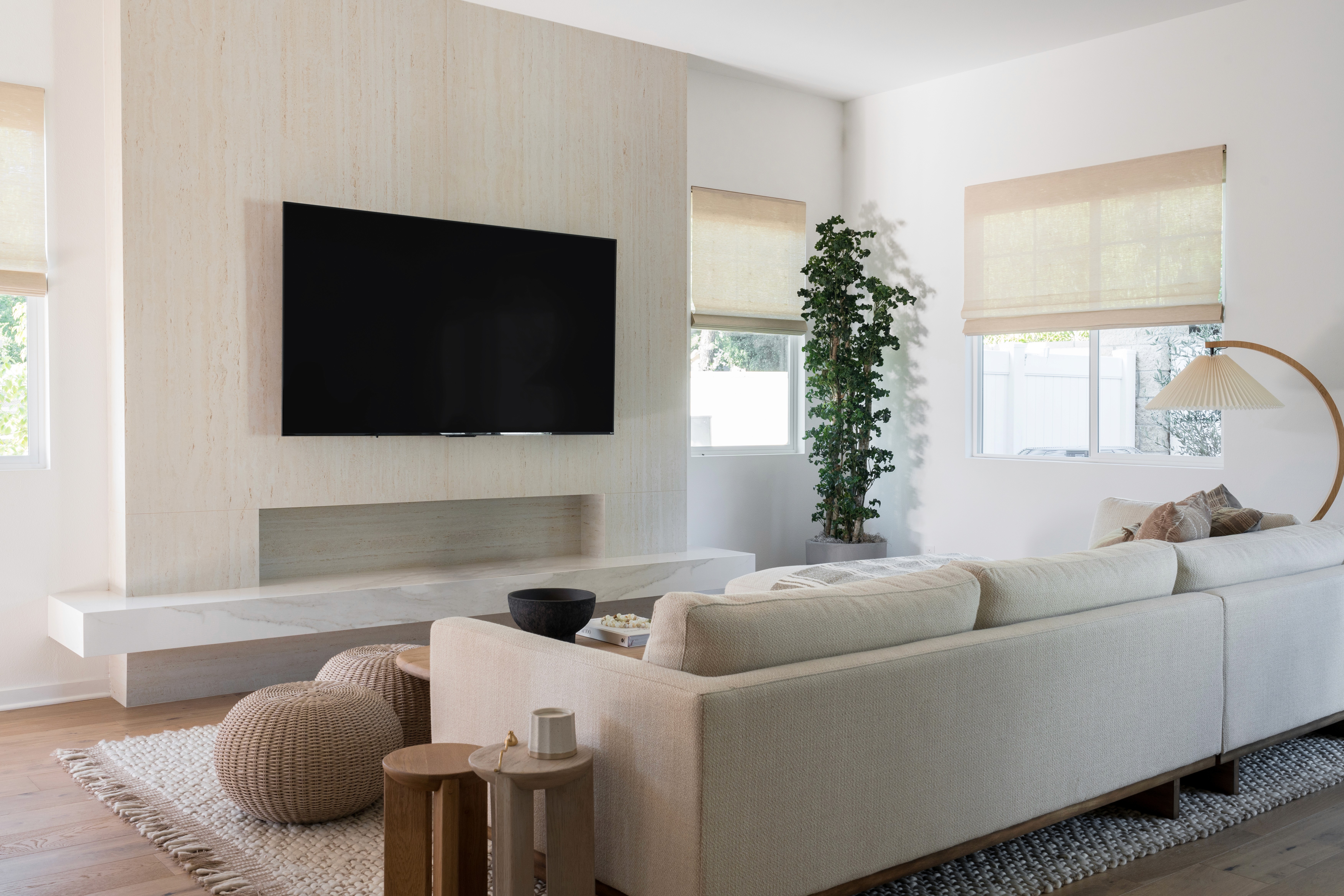 Neutral living room with travertine media wall, marble mantle, neutral roman shades by Jubilee Interiors in Arcadia, California