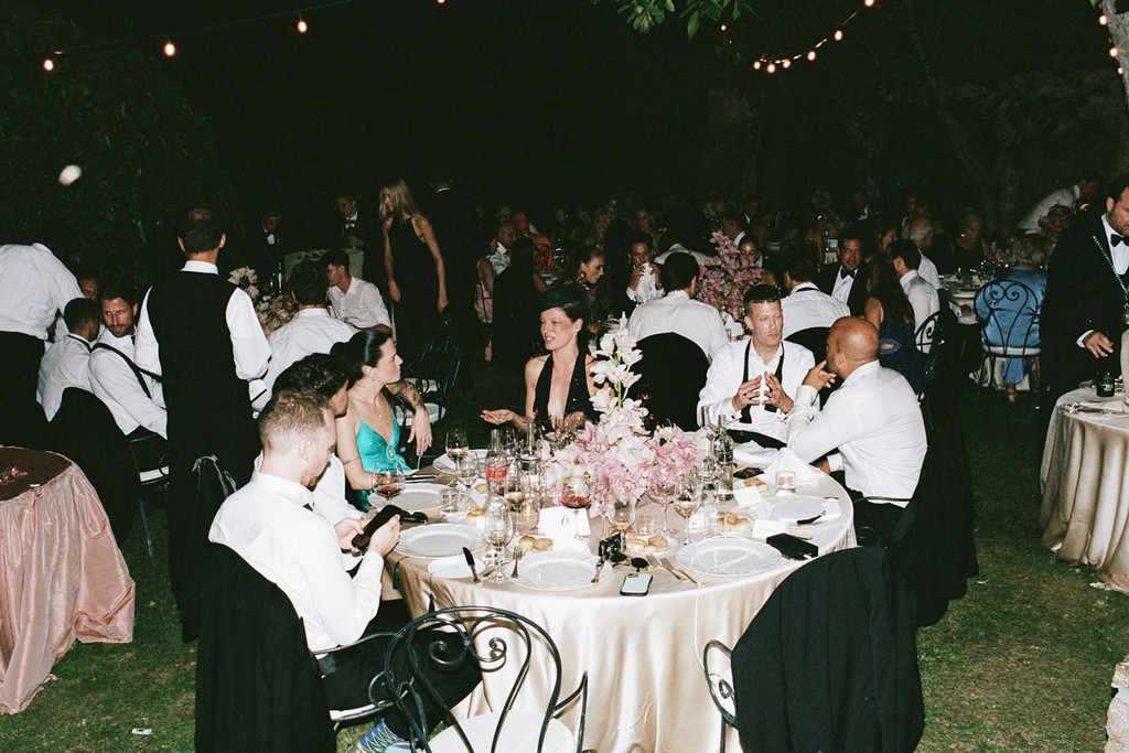 Outdoor wedding dinner with guests seated at long tables under string lights at night