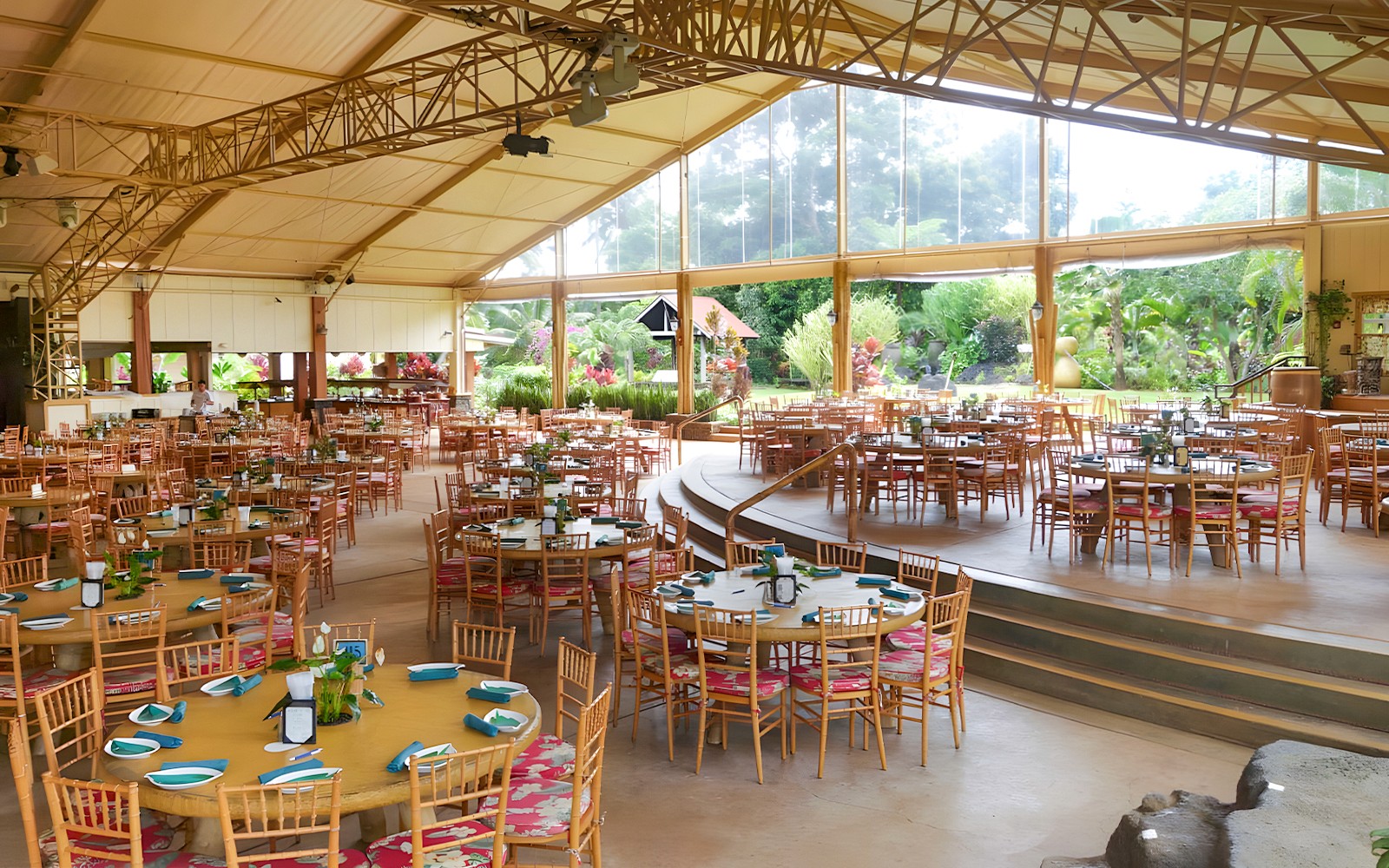 Open-air dining area set for a Hawaiian buffet luau feast with tropical garden views.