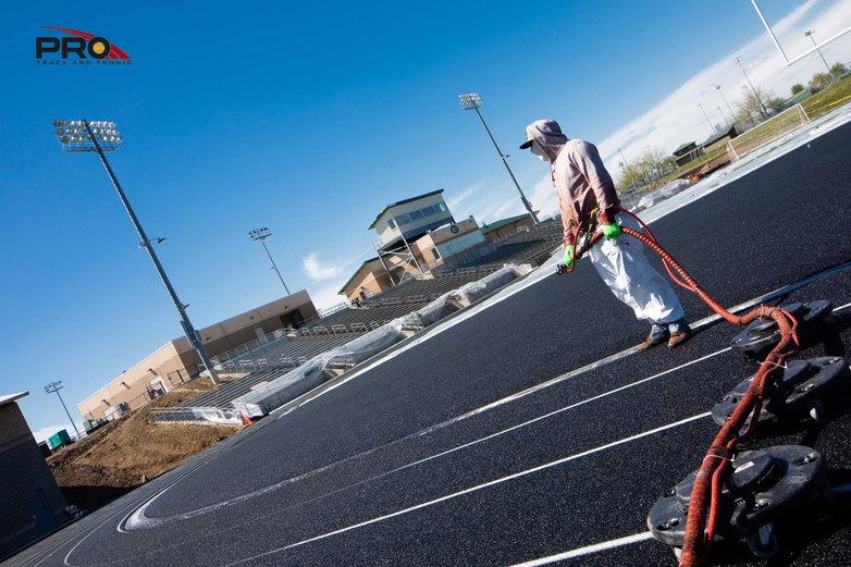 Running track maintenance work in progress, with a crew member applying surface treatment as part of a professional assessment.