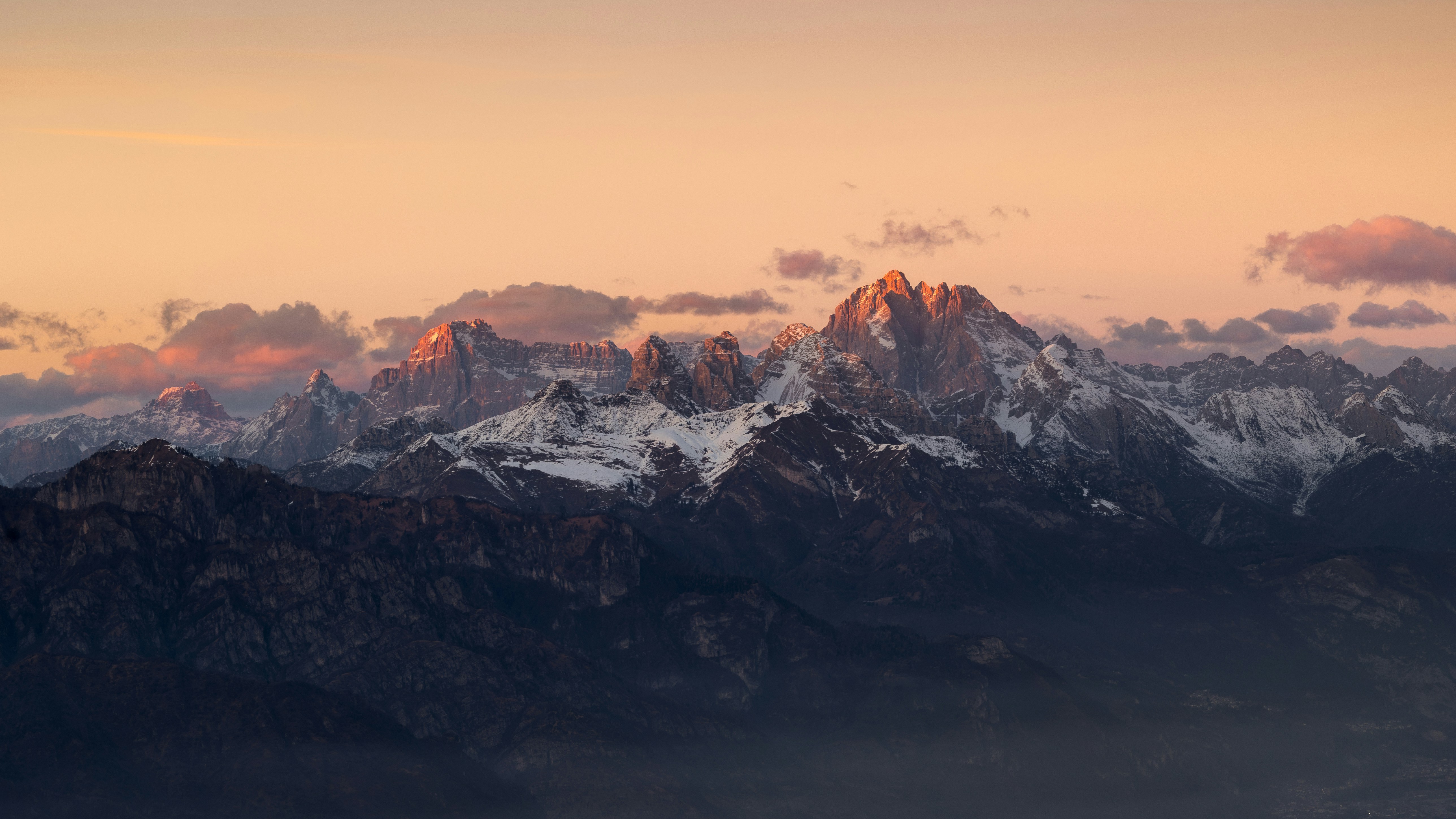 Golden light illuminates rugged snow-capped mountains during sunset.