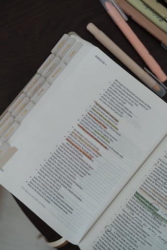 Nahaufnahme einer aufgeschlagenen Bibel mit farbigen Markierungen und handschriftlichen Notizen; daneben liegen Textmarker.